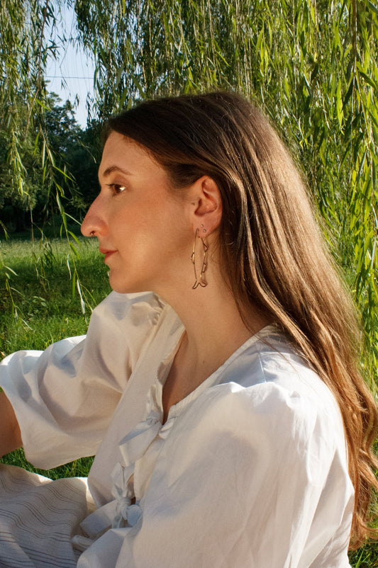Woman in a white shirt sitting outdoors with greenery in the background